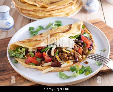 Crêpe savoureuse remplie de bœuf haché épicé, de fromage, de haricots, de laitue et de tomates. Nappés de crème sure et servis sur une assiette. Cuisine Tex mex Banque D'Images