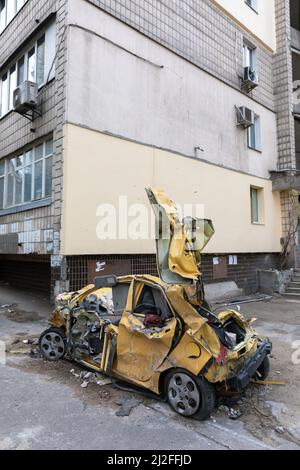 KIEV, UKRAINE - 31 mars 2022 : la guerre en Ukraine. Voiture de tourisme cassée et mutilée près d'un bâtiment résidentiel endommagé par des débris qui tombent après une attaque à la roquette russe sur Kiev Banque D'Images