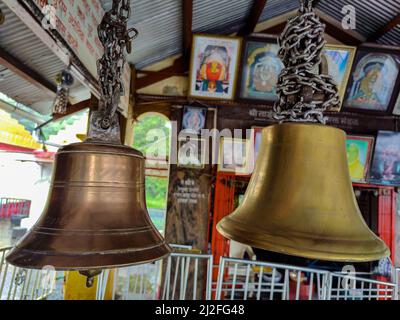 Un gros plan de deux cloches métalliques accrochées dans le temple hindou contre les photos sur les murs. Kolhapur, Inde. Banque D'Images