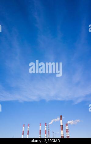 Cheminées industrielles rouges blanches et rayées de la Cogeneration urbaine moderne sont sous ciel bleu, photo verticale Banque D'Images