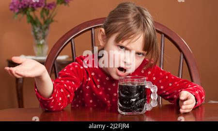 Petite fille assise à une table de café avec une tasse de café noir à la recherche comme elle cant service ou redoutant la journée est Banque D'Images