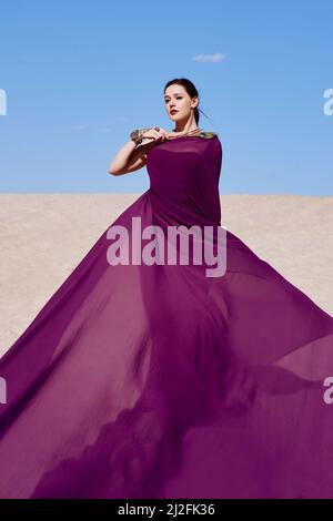 Magnifique femme brune avec la plume de paon en tissu violet dans le désert. Oriental, indien, mode, concept de style Banque D'Images