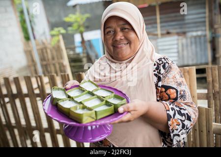 Une femme présente des gâteaux de riz doux fraîchement préparés enveloppés de feuilles de banane sur l'île de Karampuang, Sulawesi Ouest, Indonésie, Asie. Banque D'Images