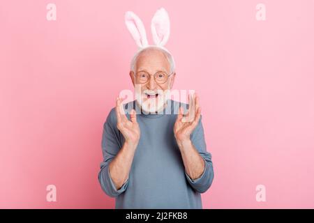 Photo de drôle impressionné homme retraité homme gris chandail lunettes lapin oreilles levant bras isolé couleur rose fond Banque D'Images