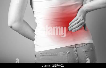 Mal de dos. Femme tenant le bas du dos douloureux avec point rouge gros plan. Sport, blessures domestiques, maladies chroniques. Syndrome de bureau. Concept de soins de santé et de médecine. Photo de haute qualité Banque D'Images