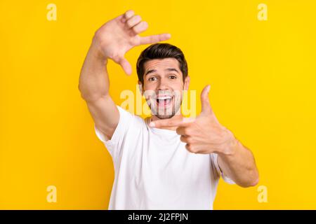 Photo du jeune garçon brunet impressionné ne photo porter t-shirt blanc isolé sur fond jaune Banque D'Images