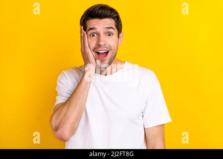 Photo du brunet millénaire impressionné gars paumes visage porter un t-shirt blanc isolé sur fond jaune Banque D'Images