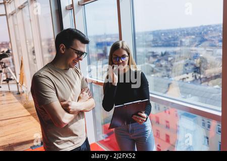 Une jeune femme d'affaires avec des documents en lunettes se tient avec un Manager tout en tenant une réunion d'affaires dans un bureau moderne. Affaires moi Banque D'Images