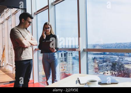 Une jeune femme d'affaires avec des documents en lunettes se tient avec un Manager tout en tenant une réunion d'affaires dans un bureau moderne. Affaires moi Banque D'Images