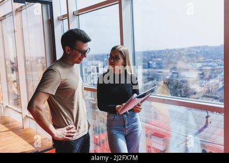 Une jeune femme d'affaires avec des documents en lunettes se tient avec un Manager tout en tenant une réunion d'affaires dans un bureau moderne. Affaires moi Banque D'Images