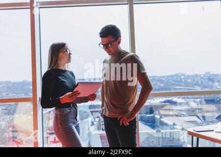 Une jeune femme d'affaires avec des documents en lunettes se tient avec un Manager tout en tenant une réunion d'affaires dans un bureau moderne. Affaires moi Banque D'Images