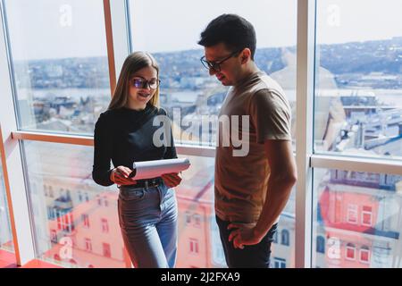 Une jeune femme d'affaires avec des documents en lunettes se tient avec un Manager tout en tenant une réunion d'affaires dans un bureau moderne. Affaires moi Banque D'Images