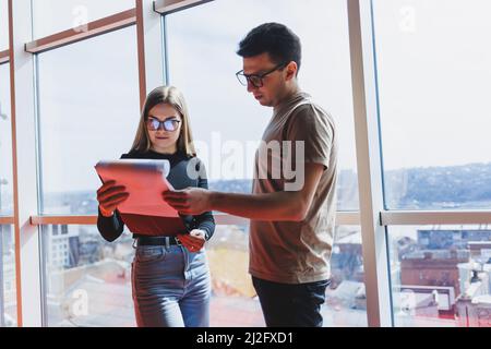 Une jeune femme d'affaires avec des documents en lunettes se tient avec un Manager tout en tenant une réunion d'affaires dans un bureau moderne. Affaires moi Banque D'Images