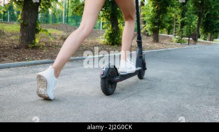 E-bike, sécurité des scooters. Jeune femme pieds à cheval dans un environnement urbain de près. Femme à la mode en scooter électrique dans le parc de la ville Banque D'Images