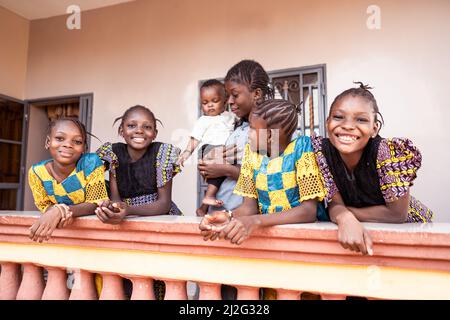 Mère d'Afrique de l'Ouest tenant un petit garçon mignon, entouré par ses quatre belles filles gaies vêtues pour la célébration. Banque D'Images