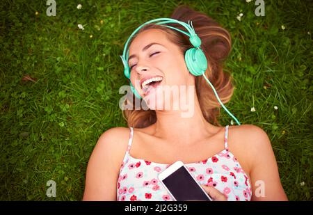 Cette chanson me rend si heureuse Photo d'une jeune femme qui écoute de la musique tout en étant allongé sur l'herbe. Banque D'Images