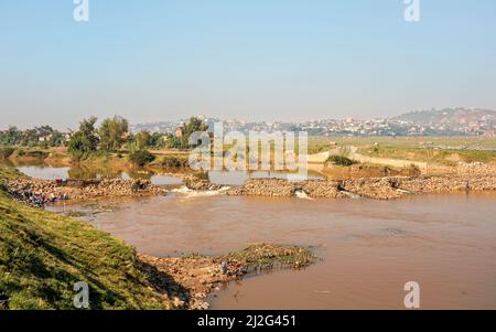 Antananarivo, Madagascar - 07 mai 2019: Personnes travaillant près de la rivière par beau temps - faire de la lessive, de la pêche, des maisons à la colline en arrière-plan Banque D'Images