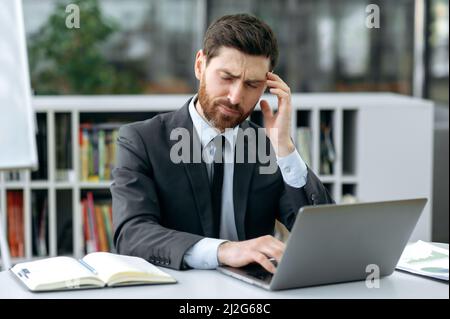 Surtravaillé, fatigué, homme d'affaires caucasien, propriétaire de l'entreprise, consultant financier, s'assoit à un bureau devant un ordinateur portable, ferme les yeux, a un mal de tête, moque le temple, a besoin d'un repos ou d'une pause Banque D'Images
