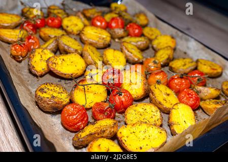 Pommes de terre et tomates cerises cuites sur une plaque de cuisson sur la table. Banque D'Images