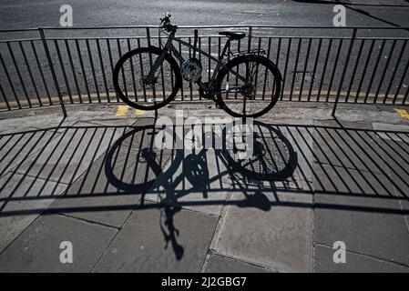 Vélo attaché à la rambarde a jeté un shodow sur la chaussée à Édimbourg, Écosse, Royaume-Uni. Banque D'Images