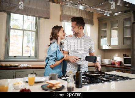 Essayez-vous de marquer des points de brownie ? Prise de vue d'une jeune femme qui embrasse son partenaire pendant qu'il prépare le petit déjeuner. Banque D'Images