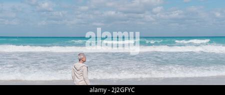Femme caucasienne âgée avec cheveux gris courts seule sur la plage de sable de l'océan Atlantique, Cuba. Banque D'Images