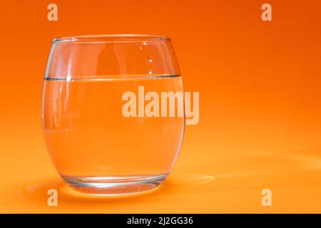 Gobelet en verre avec eau purifiée sur fond orange et orange clair. Copier l'espace Banque D'Images