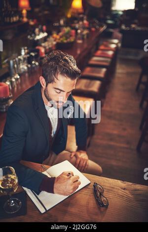 Tout commence par un tracé. Photo en grand angle d'un jeune homme assis avec son journal dans un bar. Banque D'Images