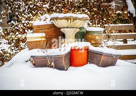 pots de fleurs extérieurs avec plantes mortes empilées autour du mangeoire à oiseaux en béton en hiver partiellement recouvert de neige Banque D'Images