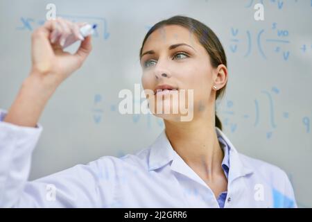 Résoudre des équations pour trouver toutes les solutions dont elle a besoin. Plan rogné d'une jeune scientifique féminine écrivant des équations sur un mur de verre dans un laboratoire. Banque D'Images