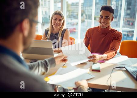 De jeunes collègues d'une commission prennent des documents d'un candidat masculin dans une atmosphère agréable lors d'une entrevue pour un emploi. Entreprise, personnes, Banque D'Images