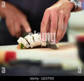 Il a l'air assez bon pour manger. Prise de vue d'un jeune homme inidentifiable préparant des sushis dans sa cuisine. Banque D'Images
