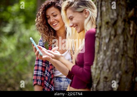 Deux jeunes filles gaies regardant le téléphone mobile et riant. Été, paysage de montagne. Liberté, amitié, concept de la nature. Banque D'Images