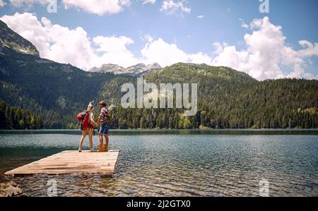 Un jeune couple se tient sur le quai au lac et profite de la vue pendant la randonnée en montagne, par une belle journée. Voyage, nature, randonnée Banque D'Images