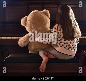 Partager ses talents avec son fandy. Vue arrière photo d'une petite fille assise devant un piano avec son ours en peluche. Banque D'Images