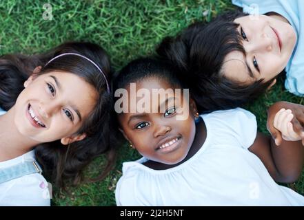 C'était une journée amusante. Photo de trois adorables enfants qui se trouvent ensemble sur la pelouse. Banque D'Images