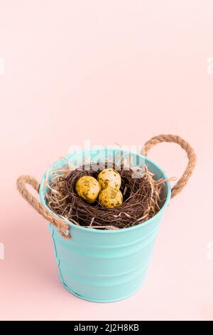 Petit seau turquoise avec nid d'œufs de caille dorés de couleur sur fond rose pastel. Carte de vœux de fête. Orientation verticale. Copier l'espace. U fictif Banque D'Images