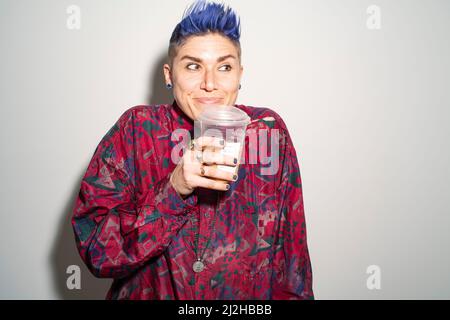 Studio portrait de la personne souriante non binaire tenant une tasse jetable Banque D'Images