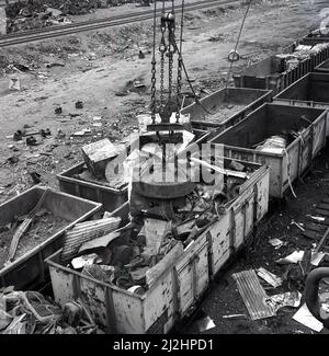 1950s, historique, un maître de sauvetage rapide - un gros aimant sur une grue - utilisé pour mettre de la ferraille d'acier et d'autres métaux jetés à une cour latérale de chemin de fer dans des wagons de fret à l'usine d'acier d'Abbey Works, Port Talbot, pays de Galles, Royaume-Uni. Un maître de sauvetage est un aimant léger utilisé pour les opérations de procession de rebut. Banque D'Images