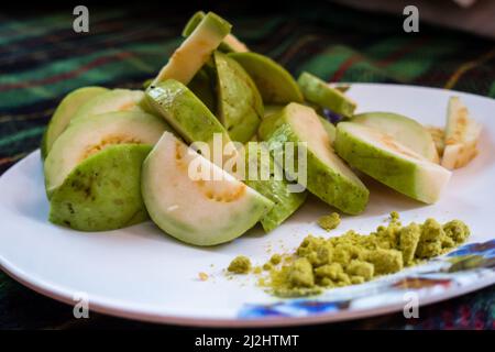 Un gros plan de salade de goyave servi avec un mélange indien de sel vert sur une assiette blanche. Banque D'Images