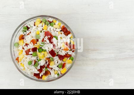 Légumes surgelés : maïs, pois verts, poivre doux et riz, dans une assiette en verre sur une table en bois Banque D'Images