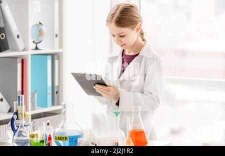 Fille pendant l'expérience de chimie scientifique de prendre des notes près de la table avec des tubes.Écolière avec équipement chimique en cours d'école Banque D'Images