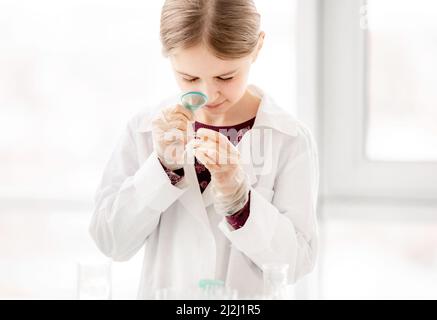 Smart girl pendant l'expérience de chimie scientifique regardant le verre avec des tests. Écolière avec équipement chimique en cours d'école Banque D'Images