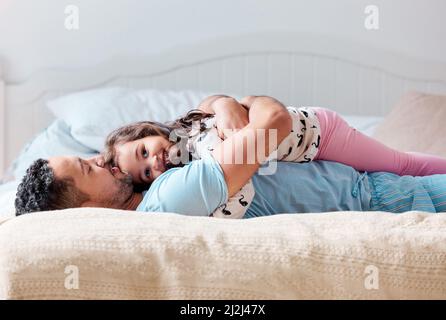 Nous commençons toujours la journée par une session de câlin. Photo d'une petite fille couchée sur la poitrine de son père à la maison. Banque D'Images