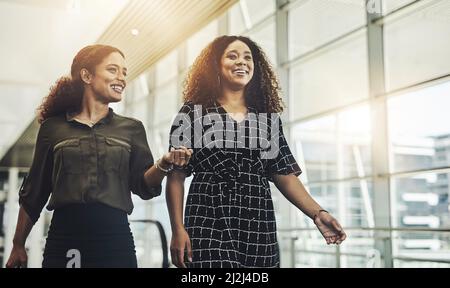 Souriez jusqu'au sommet. Photo courte de deux jeunes femmes d'affaires attirantes qui marchent dans un lieu de travail moderne. Banque D'Images