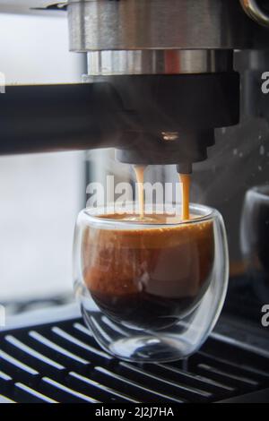 Faire du café frais sortant d'une machine à café espresso. Faire de l'expresso dans une tasse à café en verre transparent. Banque D'Images