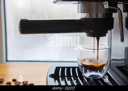 Faire du café frais sortant d'une machine à café espresso. Faire de l'expresso dans une tasse à café en verre transparent. Banque D'Images