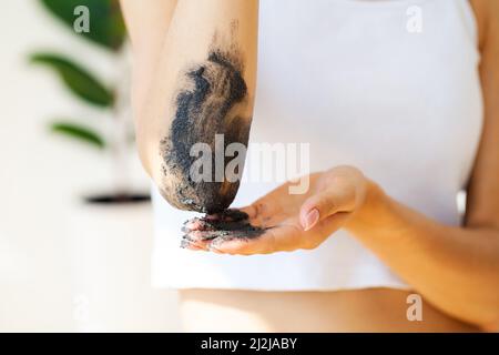 La femme nettoie la peau du corps avec un gommage au café dans la salle de bains. Banque D'Images