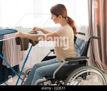 Une femme caucasienne dans un fauteuil roulant pend une lessive humide sur un sèche-linge. Banque D'Images