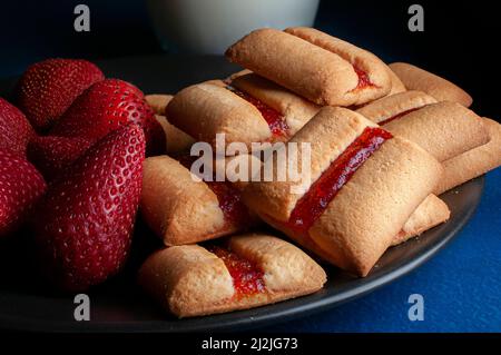 Une pile de barres à biscuits aux fraises avec un verre de lait froid et des fraises naturelles fraîches sur le côté de la nourriture sombre Banque D'Images